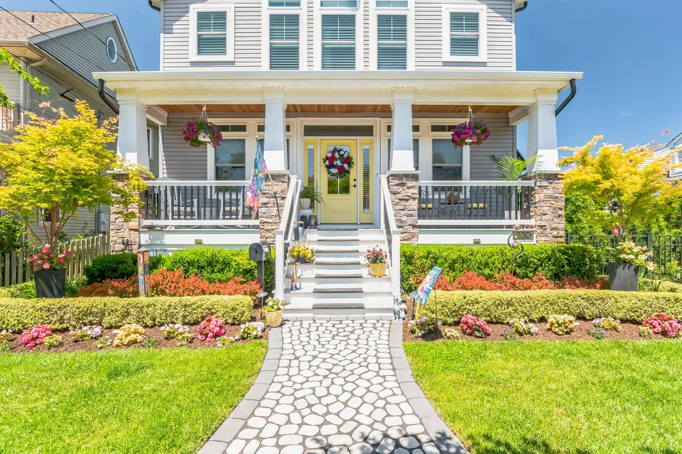 We see the front of a white house adorned by plants and flowers in Ocean City, NJ against a clear blue sky.