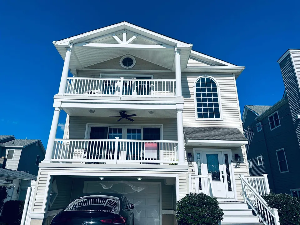 We see the front of a tall, eggshell-white house in Ocean City, NJ against a clear blue sky.