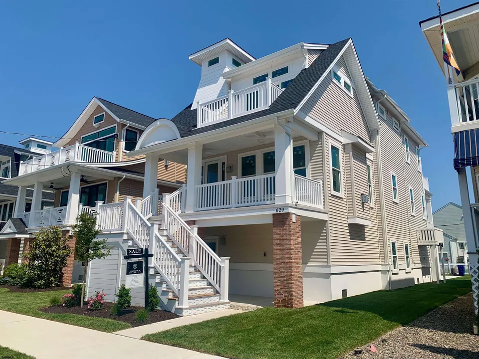 We see the front of a beige and white house in Ocean City, NJ against a clear blue sky.
